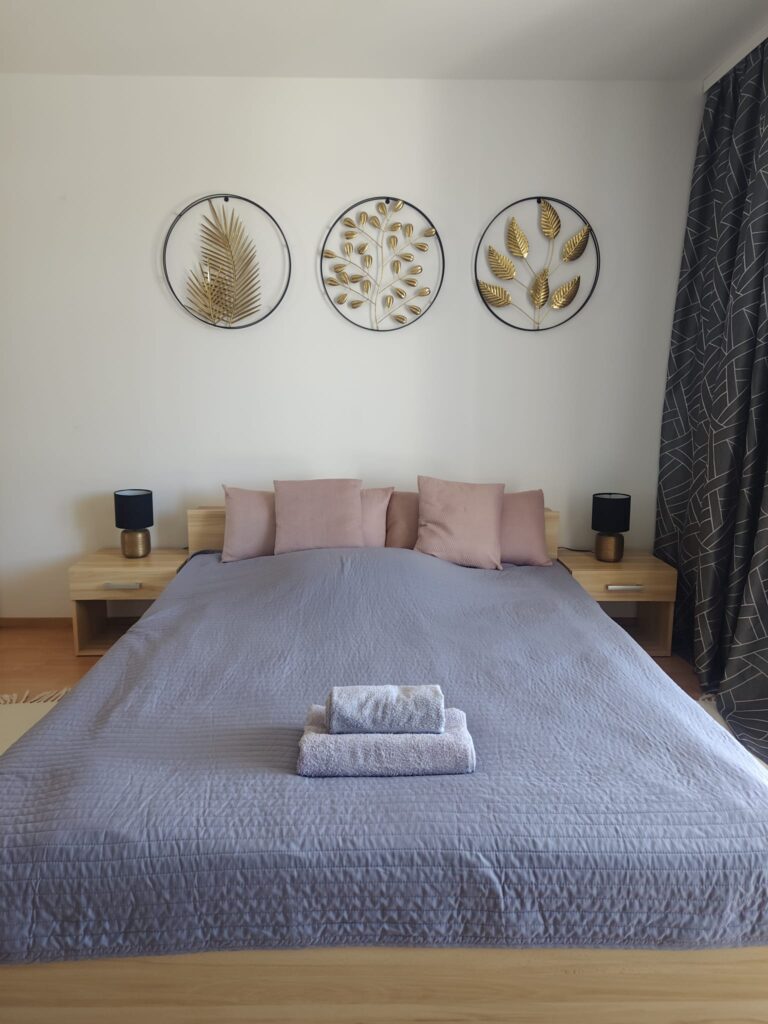 Sypialnia w apartamencie Sweet Stay z podwójnym łóżkiem, różowymi poduszkami, ręcznikami i trzema okrągłymi złotymi dekoracjami na ścianie